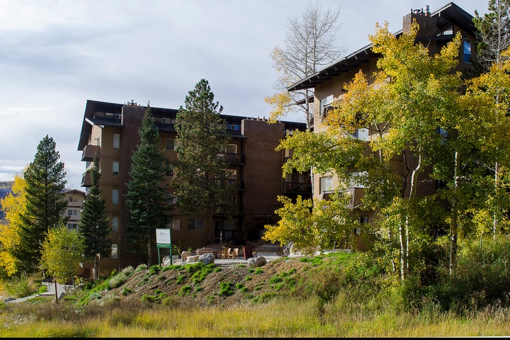 This distinctive alpine-style property sits nestled among vibrant golden aspens and evergreen pines. The multi-level building features a natural mountainside setting with seasonal autumn foliage framing the entrance.