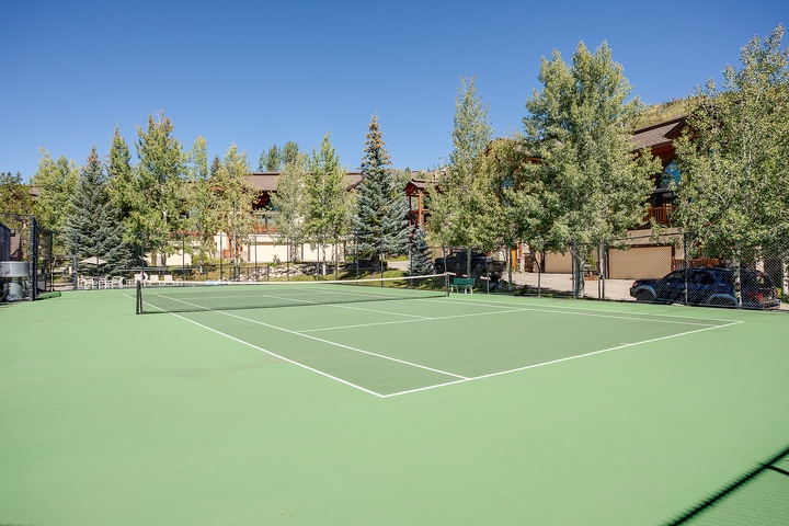 A pristine tennis court surrounded by mature evergreens and mountain-style buildings, offering guests an active outdoor amenity in a tranquil alpine setting.