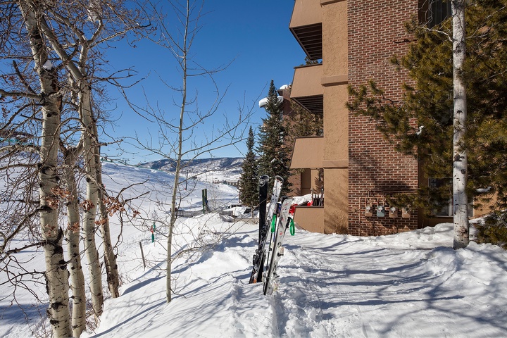 This slopeside property offers direct ski-in access, with mountain views and winter scenery framing the brick exterior. Aspen trees and evergreens line the snow-covered landscape.
