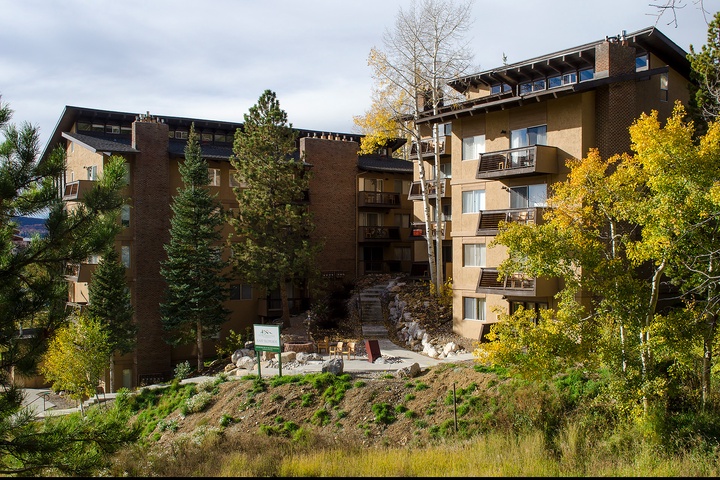 Multi-level property building surrounded by evergreens and golden aspens, nestled in a natural hillside setting with marked pathways leading to the entrance.