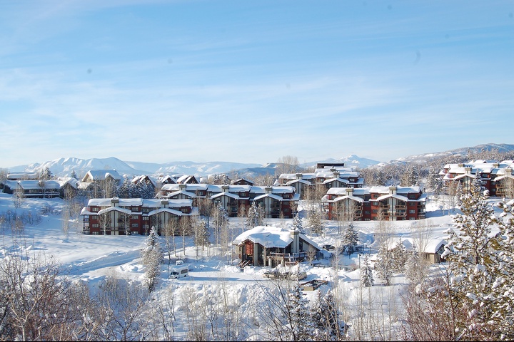 Snow-dusted vacation homes rest peacefully in a picturesque mountain valley, surrounded by pristine winter wilderness and distant peaks under clear skies.
