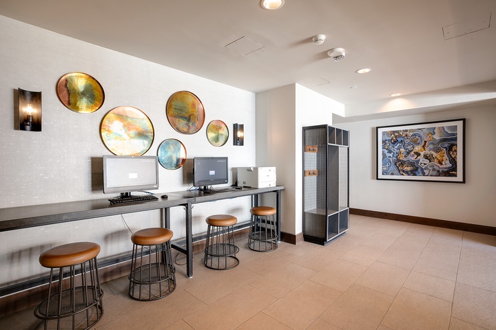 A modern business center featuring workstations with sleek desks, comfortable seating, and dual monitors. Vibrant circular art adorns the walls, creating an inspiring workspace for staying productive during your stay.