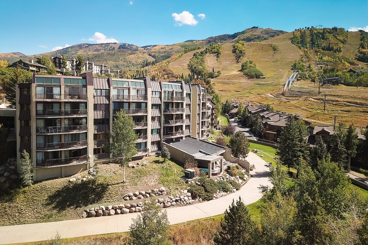Multi-level property nestled at the base of mountain slopes, surrounded by landscaped grounds and alpine scenery, offering convenient access to outdoor recreation.
