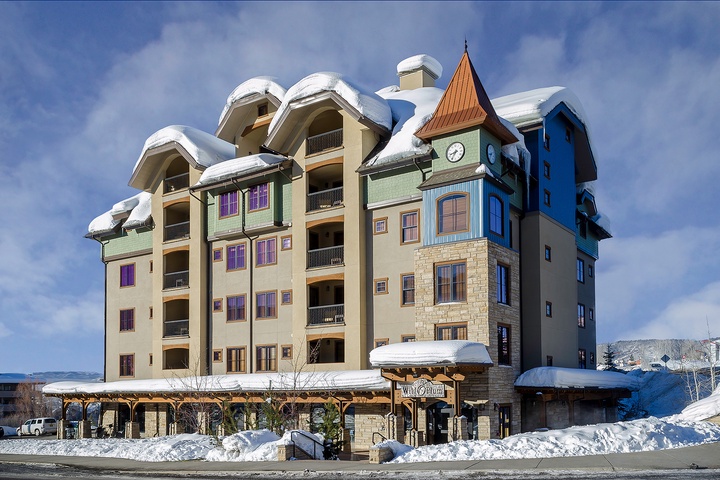 Charming alpine-inspired building nestled in a snowy mountain setting, featuring distinctive architecture with a clock tower and colorful accents.