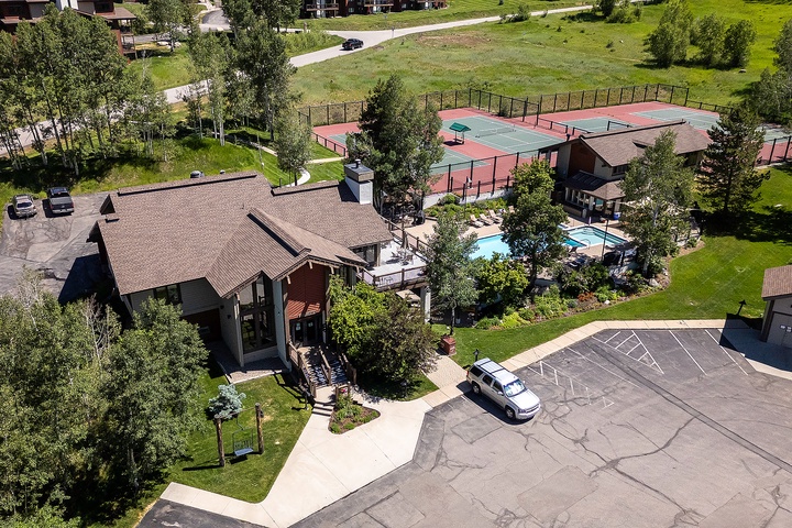 Aerial view of the property showing the main building, swimming pool area, tennis courts, and ample parking surrounded by mature trees and green lawns.