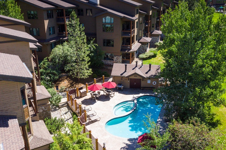 Aerial view of the resort property featuring an outdoor swimming pool surrounded by lush greenery, multi-story lodge buildings, and nearby recreational amenities.
