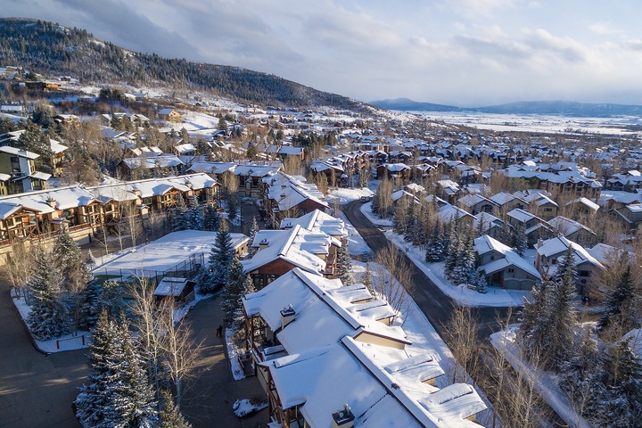Aerial view of a snow-covered mountain resort community nestled among evergreens, with the valley stretching into the distance under a serene winter sky.