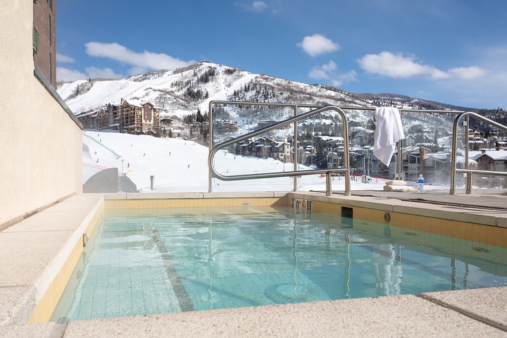 The outdoor heated pool sits adjacent to the ski slopes, with panoramic mountain views framing the winter resort landscape. Ski runs, lodges, and snowy peaks form the surrounding area's dramatic alpine backdrop.