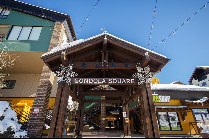 Gondola Square marks the base area entrance, with festive snowflakes and string lights welcoming guests to the mountain village on a crisp winter day.