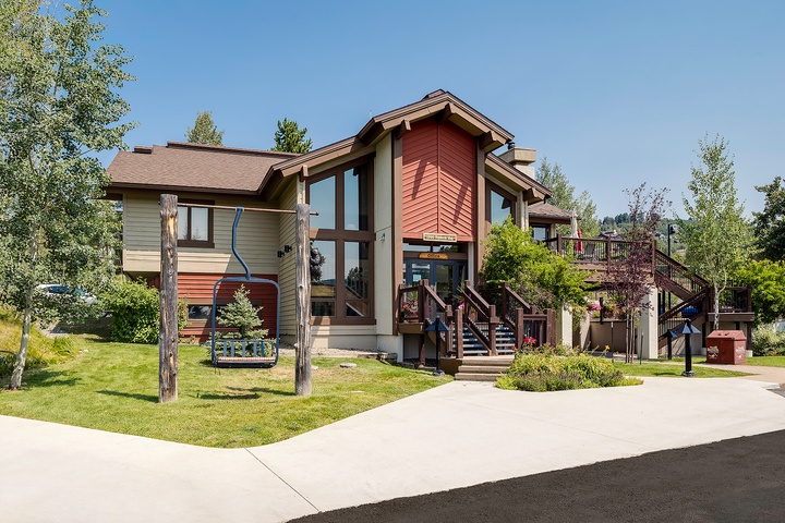 Modern mountain lodge-style building with expansive decks and natural landscaping, providing a welcoming arrival experience in a scenic area.