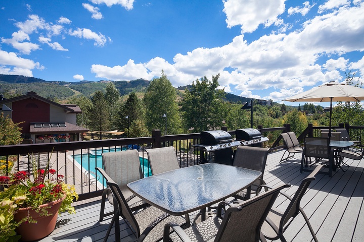 The spacious deck overlooks mountain vistas and a nearby pool, featuring multiple dining areas and twin barbecue grills ready for your outdoor gatherings.