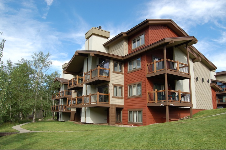 Multi-level vacation property featuring warm-toned architecture with private balconies, set on manicured green lawns surrounded by aspens and mountain views.