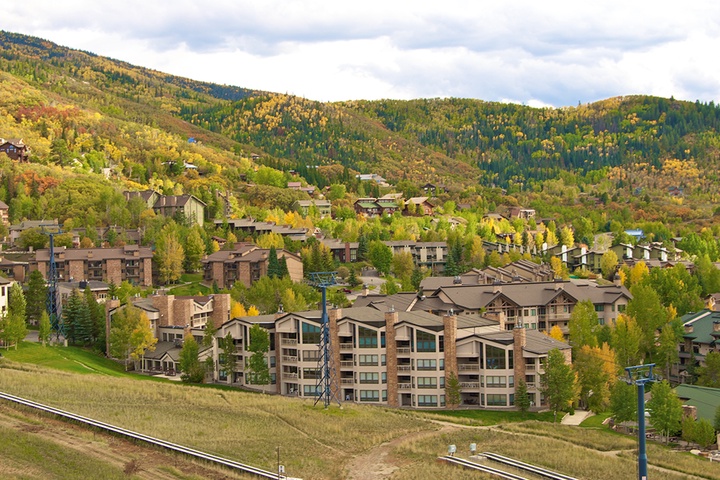 Nestled in a picturesque mountain valley, this seasonal ski resort community features lush autumn foliage, evergreen forests, and lift infrastructure set against dramatic hillside terrain.