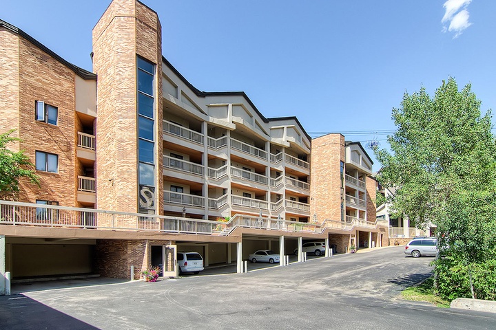 Contemporary multi-story brick building featuring covered parking, private balconies, and modern architectural design set against clear blue skies.