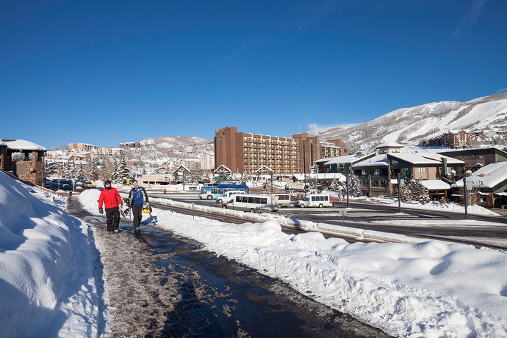 A winter resort town framed by snow-covered mountains, with ski lodges, shuttle buses, and nearby slopes visible—perfect location for a mountain getaway.