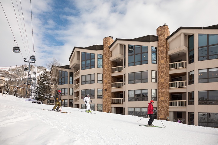 Multi-story vacation property with stone chimneys and balconies sits slope-side, offering direct ski-in/ski-out access at a mountain resort with lift visible overhead.
