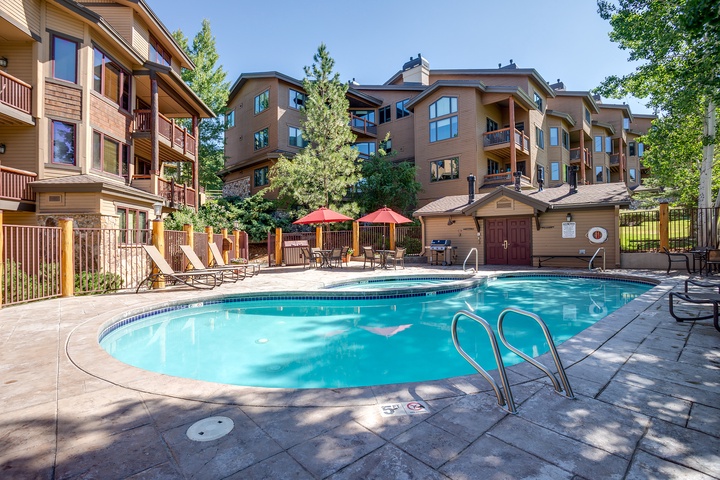 Sun-soaked pool awaits, surrounded by towering pines and mountain-style architecture. Lounge chairs and shaded seating invite relaxation after your alpine adventures, making this your perfect retreat to unwind.