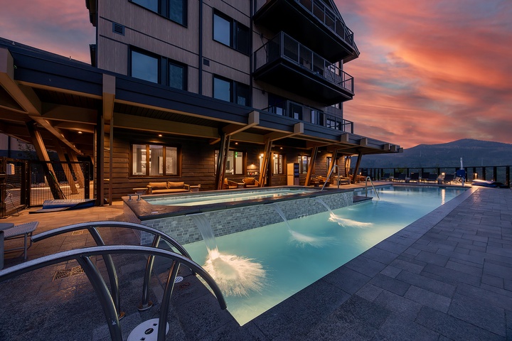 A stunning evening awaits at this modern rooftop pool area, where warm waters glow beneath a painted mountain sunset sky. Contemporary covered seating areas frame the space, perfect for relaxation after a day of adventure.