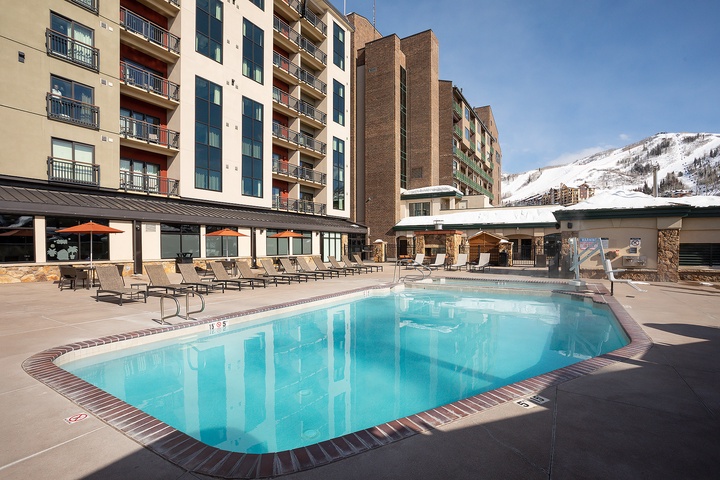 Sparkling heated pool surrounded by comfortable loungers, with dramatic mountain views providing a stunning alpine backdrop just steps from your vacation rental.
