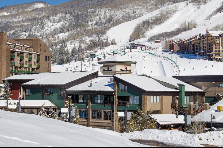 A winter ski village surrounded by snow-covered mountains, ski slopes, and lodges in a scenic alpine setting.