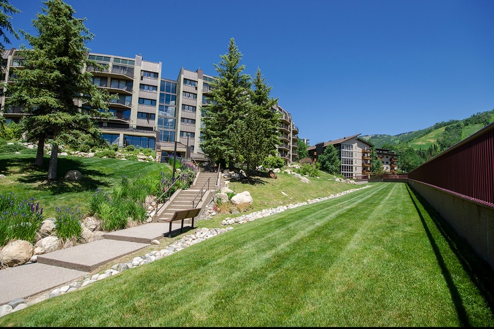 Modern property building nestled in a scenic mountain setting with lush green hillsides and manicured lawns, creating an inviting base for your stay.