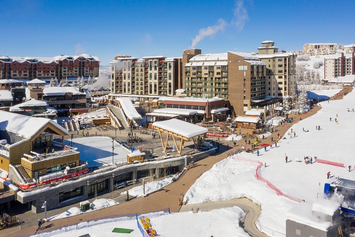 This aerial view captures the vibrant ski village base, showcasing snow-covered slopes, lodges, dining options, and entertainment facilities nestled in the heart of winter mountain scenery.