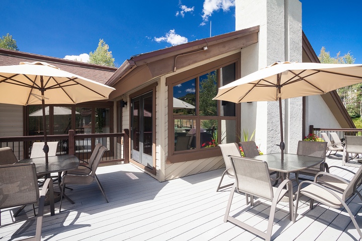 This spacious deck offers shaded seating under cream umbrellas, with mountain views and direct access to the home's bright, windowed living spaces—ideal for outdoor dining and relaxation.