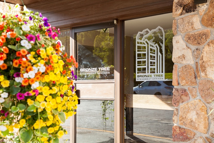 Colorful blooms greet you at the entrance, framing the property's welcoming glass doors and stone facade. A bright, cheerful arrival awaits your vacation stay.