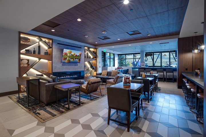 Modern communal lounge with sleek seating, a glowing fireplace, bar area, and bright windows offering scenic views—ideal for gathering and unwinding.