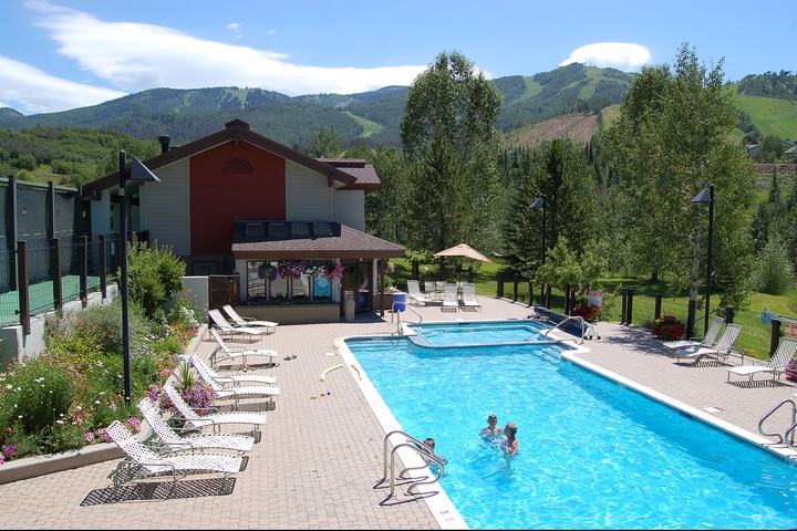 Mountain resort pool area surrounded by lush greenery and scenic peaks, offering relaxation and recreational swimming in a beautiful alpine setting.