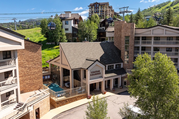 Mountain resort property in a year-round recreation area, with ski lifts and green slopes visible in the surrounding landscape. Summer-season exterior view of the building and its location.