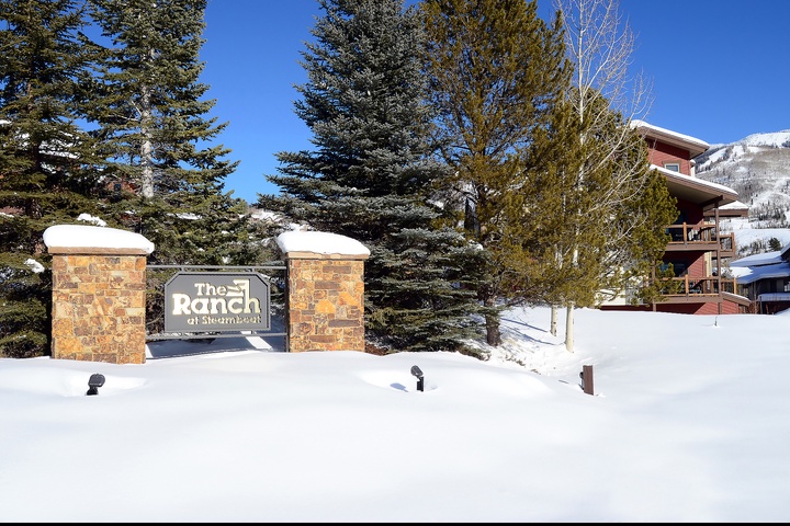 The Ranch at Steamboat entrance welcomes visitors with stone pillars and signage, surrounded by snow-dusted evergreens and mountain views in a picturesque alpine setting.