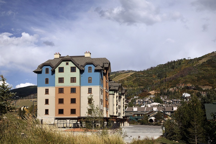A distinctive mountain resort building with colorful pastel facades set against forested alpine slopes and a dramatic sky.