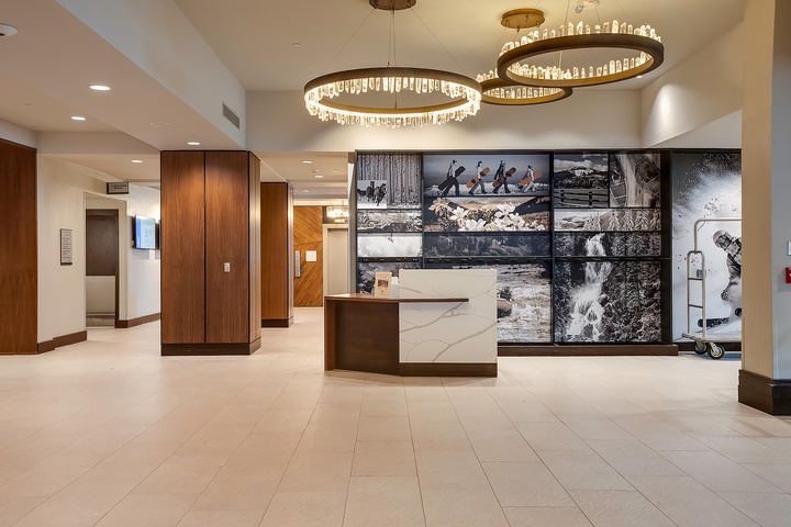 The hotel lobby welcomes arrivals with elegant circular chandeliers, polished tile floors, and striking wall art showcasing outdoor adventure scenes, setting a sophisticated yet inviting tone.
