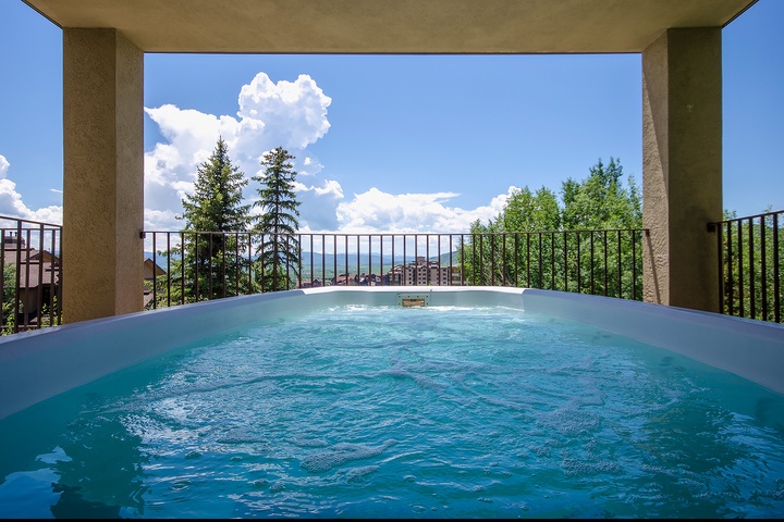 A private hot tub framed by mountain vistas, where you can soak beneath open skies, surrounded by evergreen peaks and fluffy clouds drifting overhead.