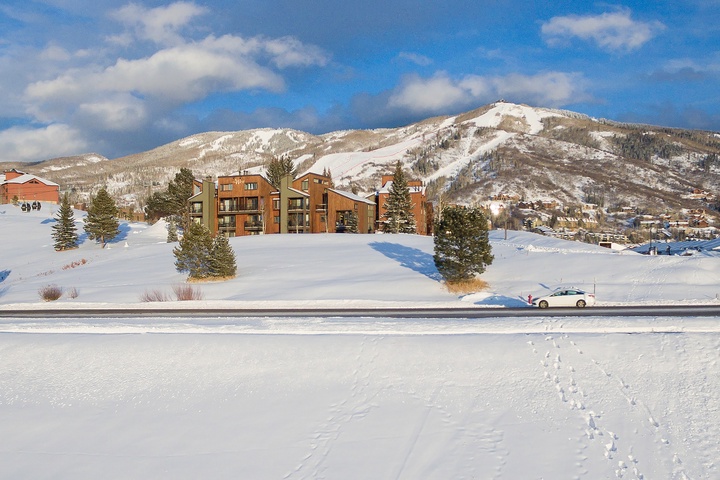 Snow-covered mountain property nestled among evergreens with scenic ski slopes in the surrounding alpine landscape.