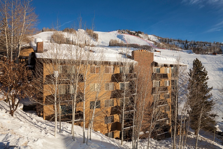 The property sits slopeside with ski runs visible in the background, framed by snow-covered aspens and surrounded by winter mountain scenery under a clear blue sky.