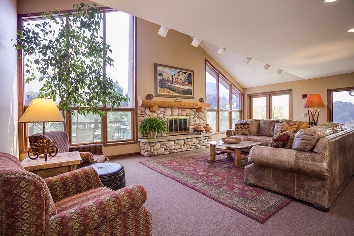 Sink into plush sofas by the stone fireplace and let natural light from floor-to-ceiling windows warm your mountain retreat—your perfect spot to unwind after a day exploring.