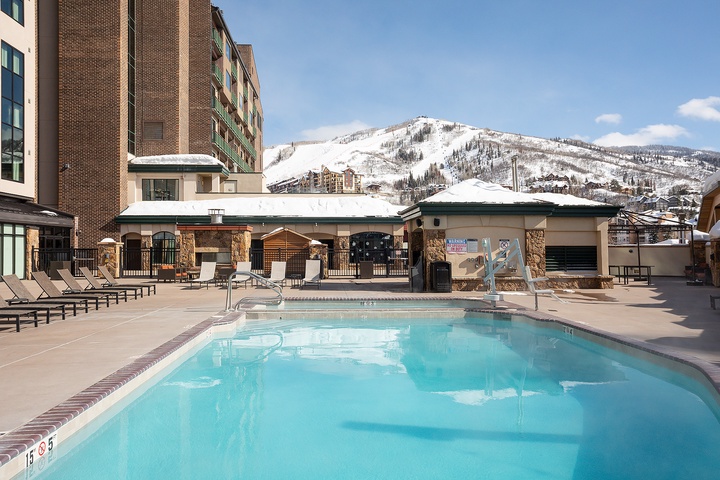 An inviting outdoor pool with sun loungers sits at the base of snow-covered slopes, offering a perfect spot to unwind after skiing.