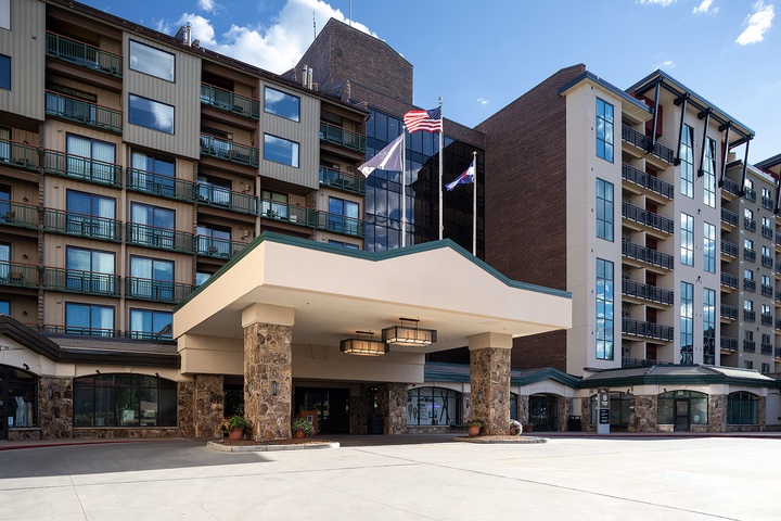 Multi-story property with stone-columned entrance, balconies on each level, and flags welcoming guests to the main building.