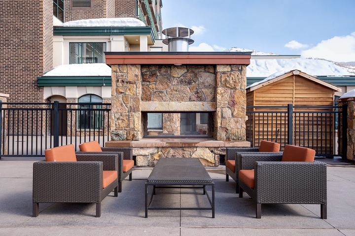 Mountain vistas frame this rooftop terrace featuring a stone fireplace, plush wicker seating, and modern comforts—your alpine escape awaits.