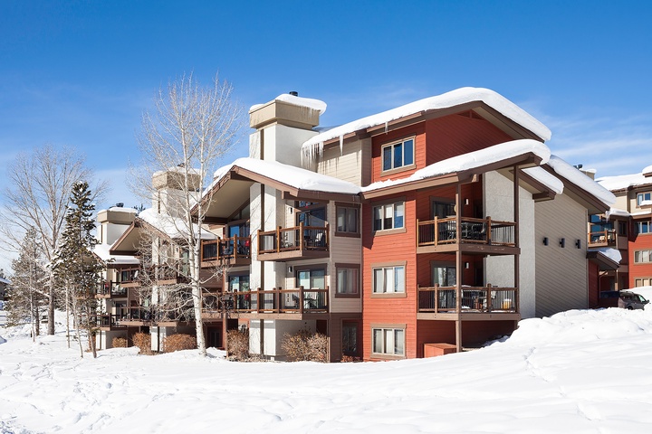 A snow-covered mountain retreat with warm wood tones and expansive balconies, offering winter getaway charm surrounded by pristine evergreens and ski country beauty.