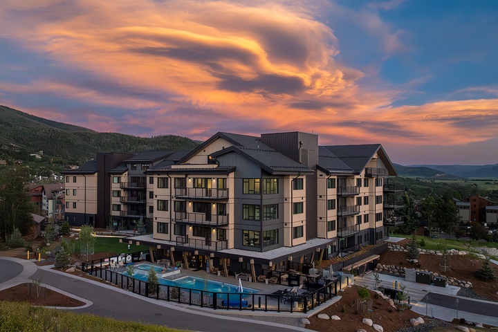 This mountain property welcomes guests with sweeping views of forested slopes and valley landscapes, set beneath dramatic alpine skies at day's end.