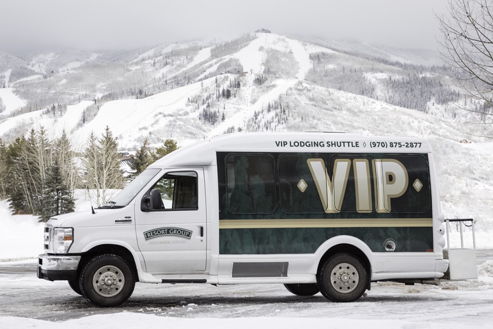 VIP shuttle ready to transport guests against a dramatic winter mountain backdrop covered in fresh snow and skiing terrain.