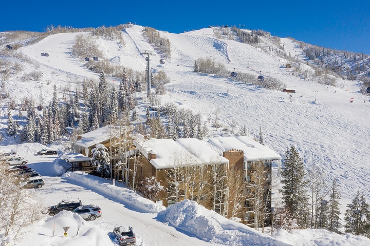 Aerial view of the property nestled at the base of ski slopes, with direct access to chairlifts and winter mountain terrain. The surrounding area offers pristine snow-covered peaks and ski runs.