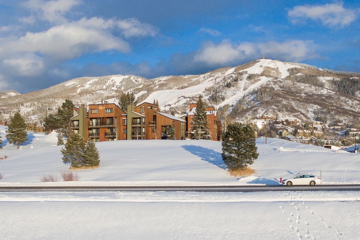 Modern mountain lodges nestled against pristine snow-covered peaks, perfectly positioned for winter adventures. The property sits in a scenic alpine valley with ski slopes visible in the distance.