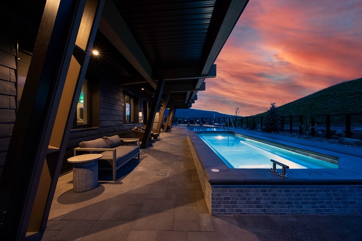 The property rests at the edge of a pristine mountain landscape, where vibrant sunsets paint the sky in dramatic shades of pink and orange above forested peaks.