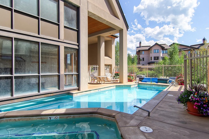 A sparkling indoor-outdoor pool area where you can swim year-round, with a hot tub, lounge chairs, and vibrant gardens under open skies.