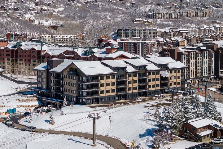 An aerial view capturing the property nestled within a snow-covered mountain resort village, with ski slopes and surrounding lodges completing the winter landscape.