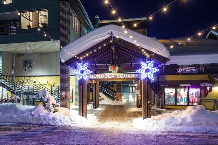 A charming winter village entrance adorned with twinkling lights and festive decorations, nestled in a snow-covered mountain setting—perfect for evening strolls and exploring nearby dining and shops.